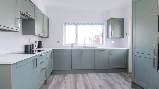 A modern kitchen with light green cabinets, a white countertop, and a window with a view of buildings outside. - 38 Clive Avenue (Lytham St. Anne's)