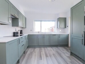 Una cocina moderna con armarios verde claro, una encimera blanca y un ventanal con vistas a edificios.