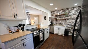 Une cuisine moderne avec des armoires blanches, une cuisinière en acier inoxydable et un mur décoratif en briques.