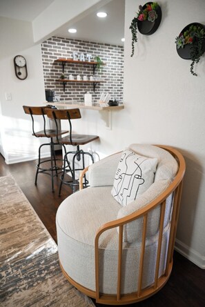 Una sala moderna con una zona de estar circular y acolchada, una mesa de comedor con sillas, una pared con diseño de ladrillo y una cocina al fondo.