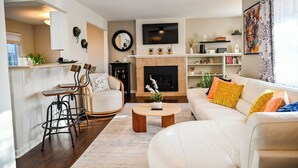 Un salon comprenant un canapé, une table basse et des fauteuils, une cheminée et un téléviseur fixé au mur.