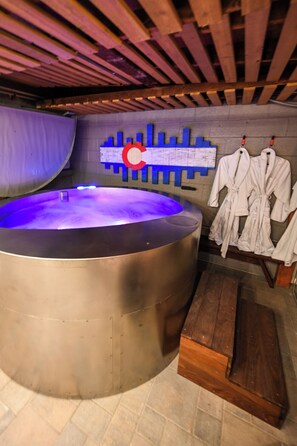 Una sauna con una vasca idromassaggio ampia, panche in legno e accappatoi bianchi su un appendiabiti.