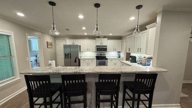 A modern kitchen with white cabinets, a central island with bar stools, and pendant lighting.