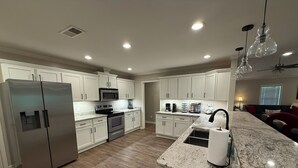 A modern kitchen with stainless steel appliances, white cabinetry, and a marble countertop.