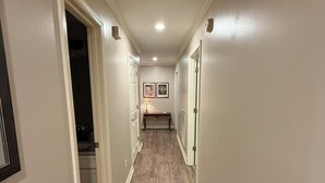 A narrow hallway with wooden flooring, white walls, and a door leading to a kitchen.