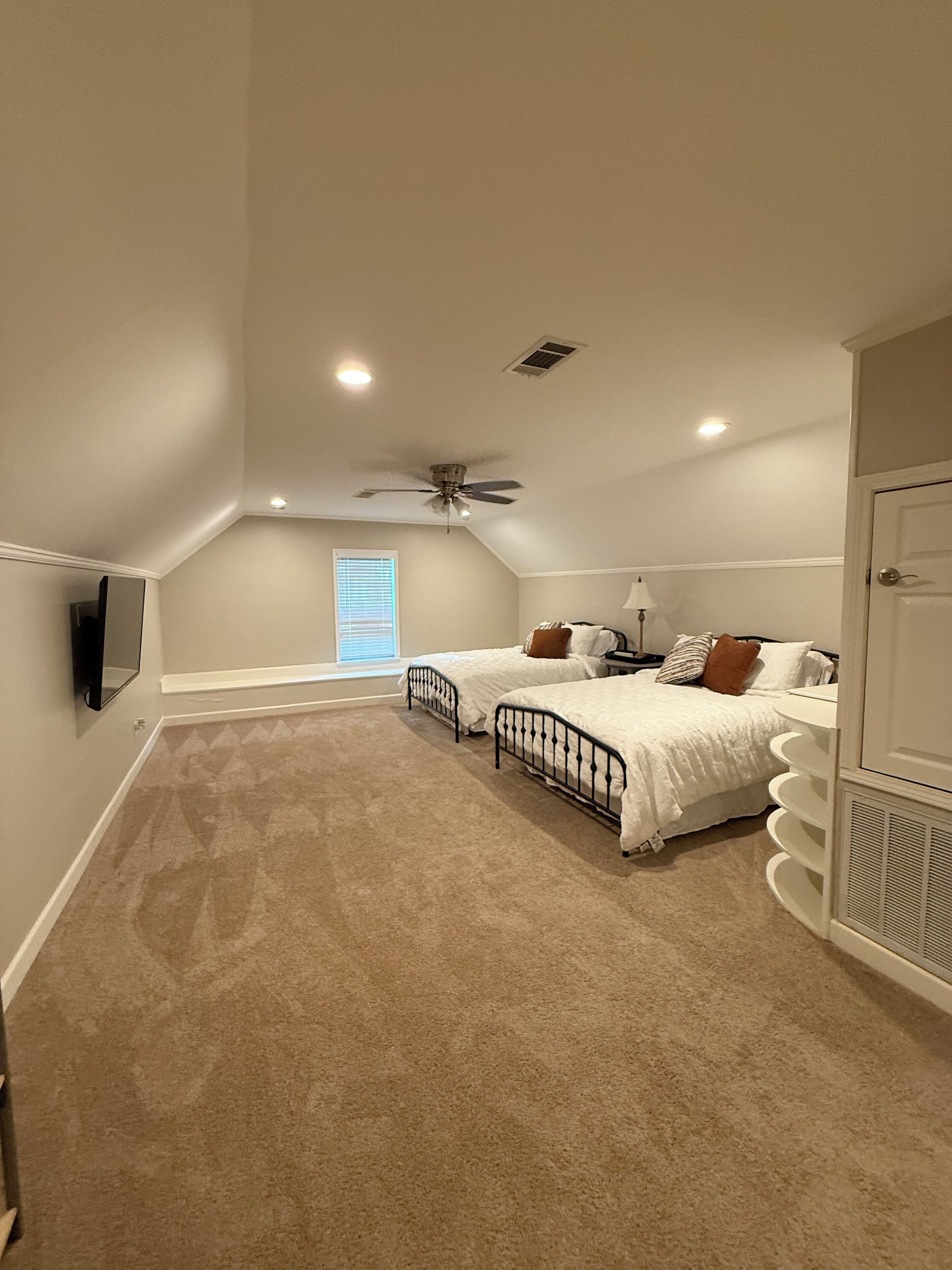 A bedroom with two beds, a ceiling fan, and a TV mounted on the wall.