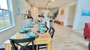 A dining area with a long wooden table set for six, surrounded by chairs.