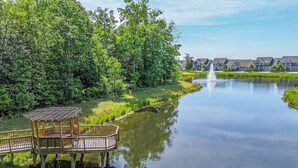 A tranquil riverside scene with a wooden gazebo and a row of houses in the background.