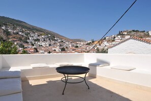 Eine Dachterrasse mit einem runden Tisch, weißen Kissen und Blick auf eine Hügelstadt.