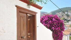 Ένα λευκό κτίριο με μια ξύλινη πόρτα και ένα μπαλκόνι στολισμένο με μοβ λουλούδια.
