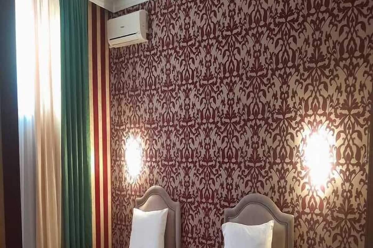 Ein Hotelzimmer mit zwei Einzelbetten, einem Vorhangfenster, strukturierten Tapeten und einer Klimaanlage.