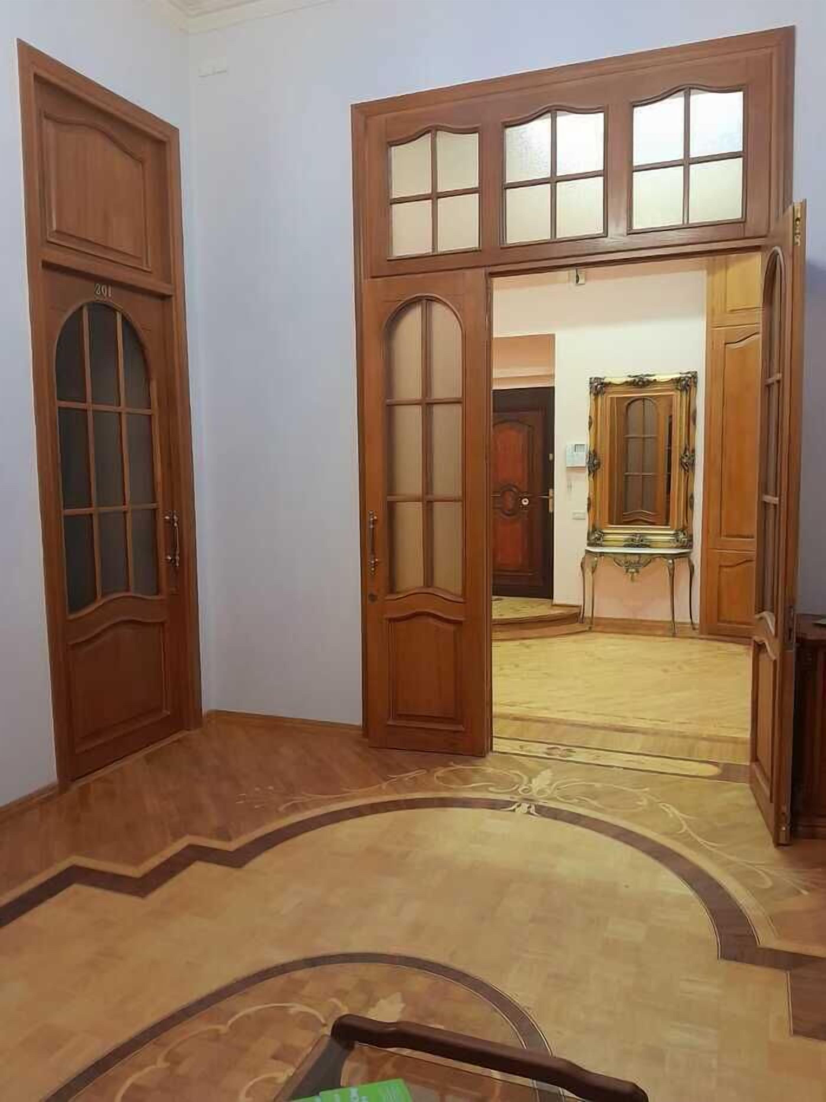 Una habitació amb una porta de fusta gran, un sòl amb moqueta i una taula petita amb una cadira.