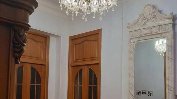 Een kamer met een kroonluchter, houten deuren, een marmeren openhaard en een spiegel.