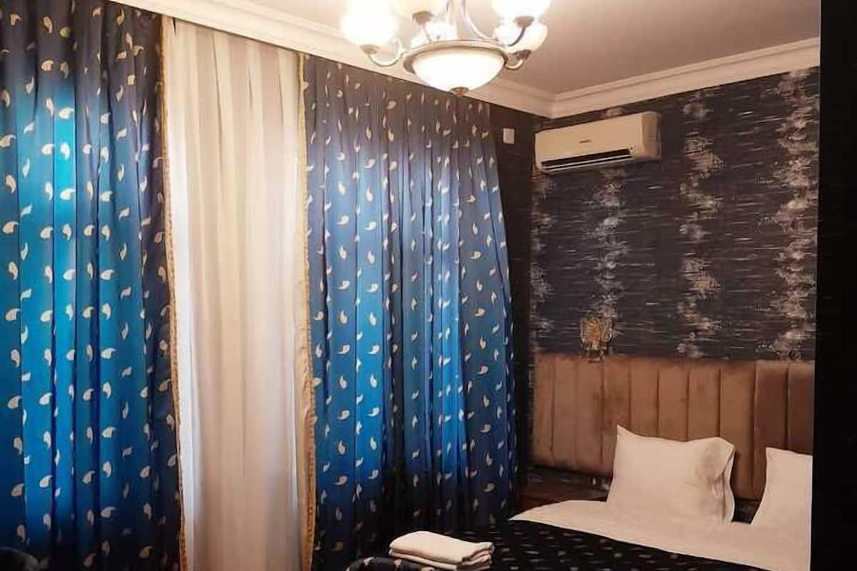 Ein Hotelzimmer mit Bett, Sessel, kleinem Tisch, einer Chandelierleuchtre und einem Vorhangfenster.