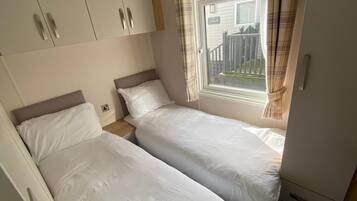 A bedroom with two single beds, a wardrobe, and a window with curtains.