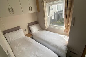 A bedroom with two single beds, a wardrobe, and a window with curtains. - Westfield Lodge Retreat (Carnforth)
