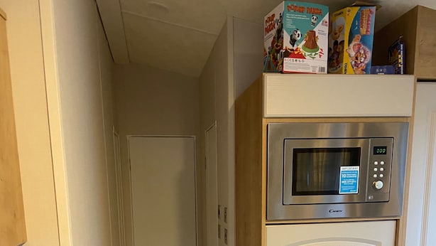 A narrow hallway with a herringbone-patterned floor, a white door at the end, and a microwave on a wooden cabinet above a white door. - Westfield Lodge Retreat-sleeps 6-pet Friendly (Carnforth)