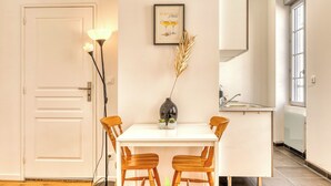 Ein Essbereich mit einem weißen Tisch und Stühlen, einer Vase mit Trockenpflanzen und einem gerahmten Bild an der Wand.