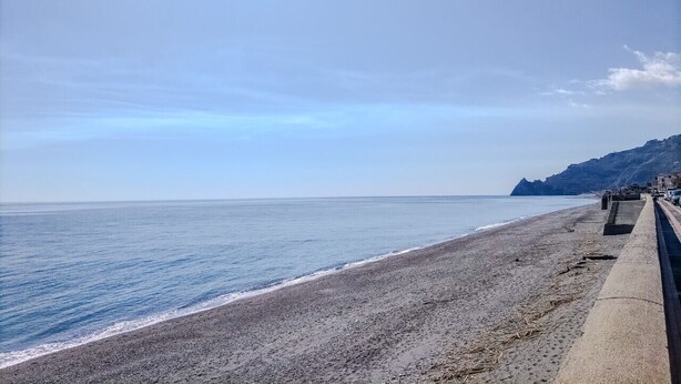 En strand med en gångväg av betong och ett berg i bakgrunden.