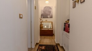 En smal hall med ett trägolv, en spegel med en dekorativ ram, en vas med torkade blommor och en matta.