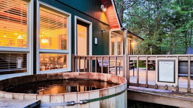 Un edificio de madera con ventanas grandes, un jacuzzi y una terraza de madera con un letrero.