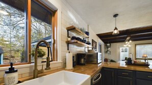 Una cocina moderna con un lavamanos grande blanco, armarios oscuros y una ventana con vistas a un jardín.