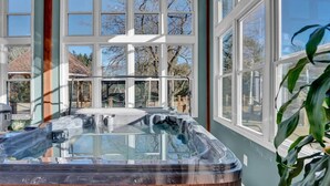Un jacuzzi en una habitación con ventanas amplias, vistas a árboles y una planta en primer plano.