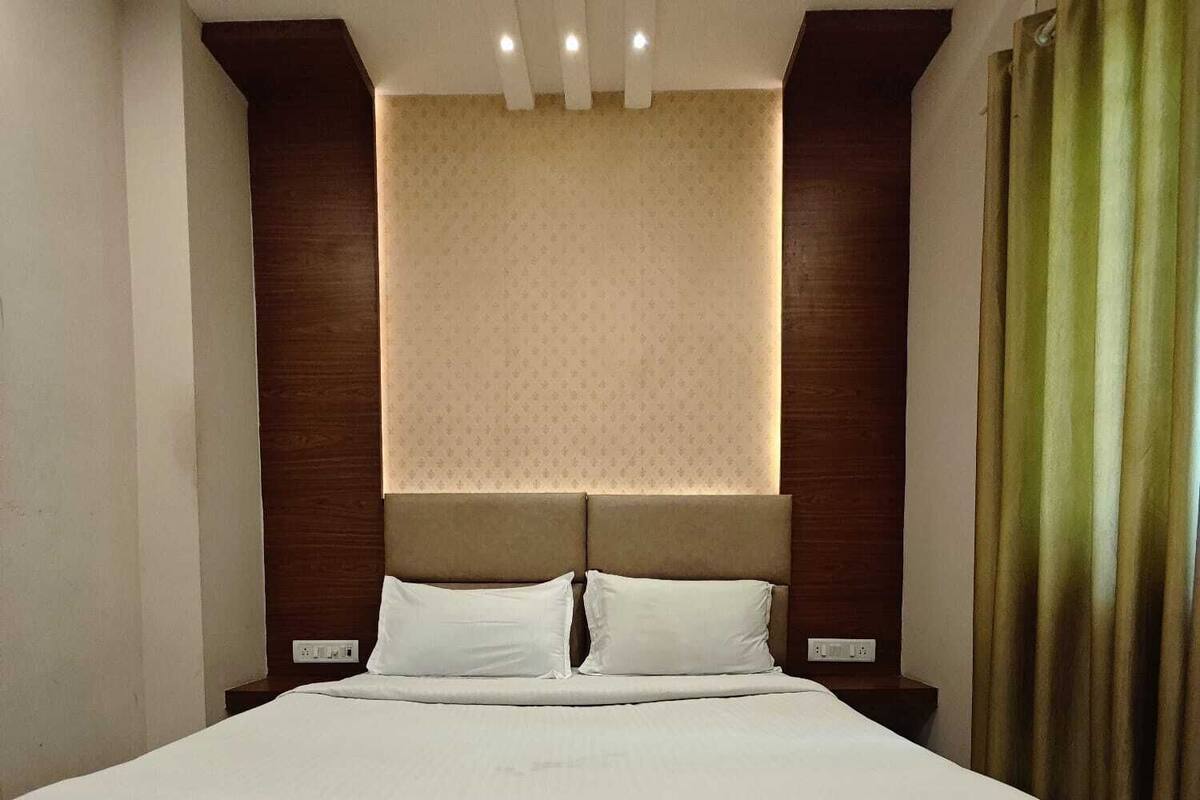 A hotel room with a large bed, a headboard with integrated lighting, and a plain wall with a subtle pattern.