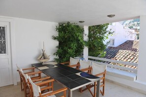 A terrace with a table and chairs, a potted plant, and a view of a tiled roof and buildings. - Dione House by GHH (Idra)