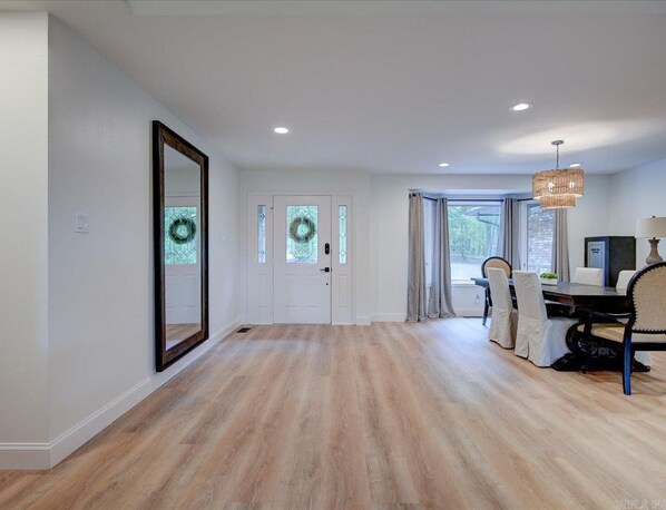 A spacious room with a wooden floor, a dining area with a table and chairs, and a large mirror on the wall.