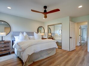 Un dormitorio con una cama grande, suelo de madera, ventilador de techo y un espejo de cuerpo entero.
