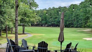 Vista de un campo de golf con sillas y una sombrilla.