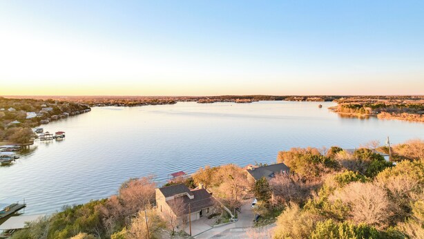 A lakeside property with a dock, a small house, and surrounding vegetation. - Luxe Lake Granbury Retreat: Dock, Deck & Game Room (Granbury)