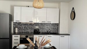 A modern kitchen with white cabinets, a stone backsplash, and a dining area set with a wooden table, white plates, and wine glasses. - Relax in the heart of the Eifel - vacation apartment with huge roof terrace (Hellenthal)