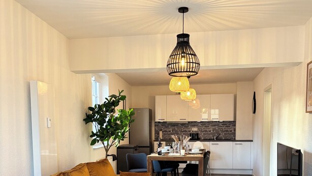 A modern living room with a sofa, a dining table, and a kitchen in the background. - Relax in the heart of the Eifel - vacation apartment with huge roof terrace (Hellenthal)