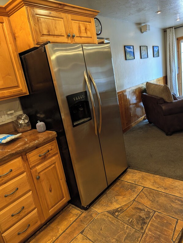 Una cocina con armarios de madera, un refrigerador de acero inoxidable, un dispensador de hielo incorporado y piso de baldosas de piedra.