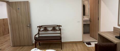 A hotel room with a bed, a wooden bench, a desk, and a bathroom visible through an open door.