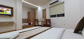 Habitación de hotel con cama, televisor montado en la pared, armario de madera, una pequeña mesa con sillas y equipo de aire acondicionado.