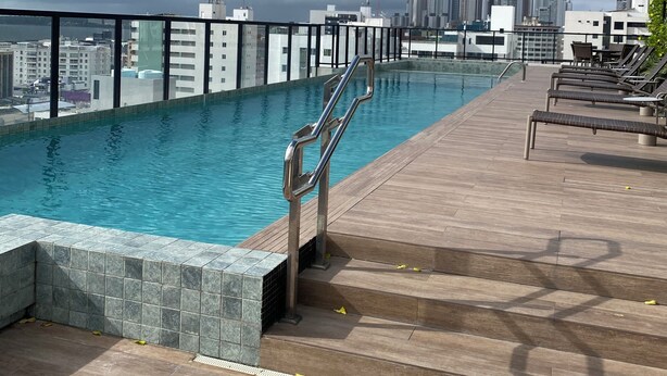 Une piscine sur le toit offrant une vue sur la ville, avec une terrasse en bois et des chaises longues.