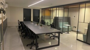 Une salle de conférence moderne, dotée d’une longue table, de chaises de bureau noires et de cloisons en verre.