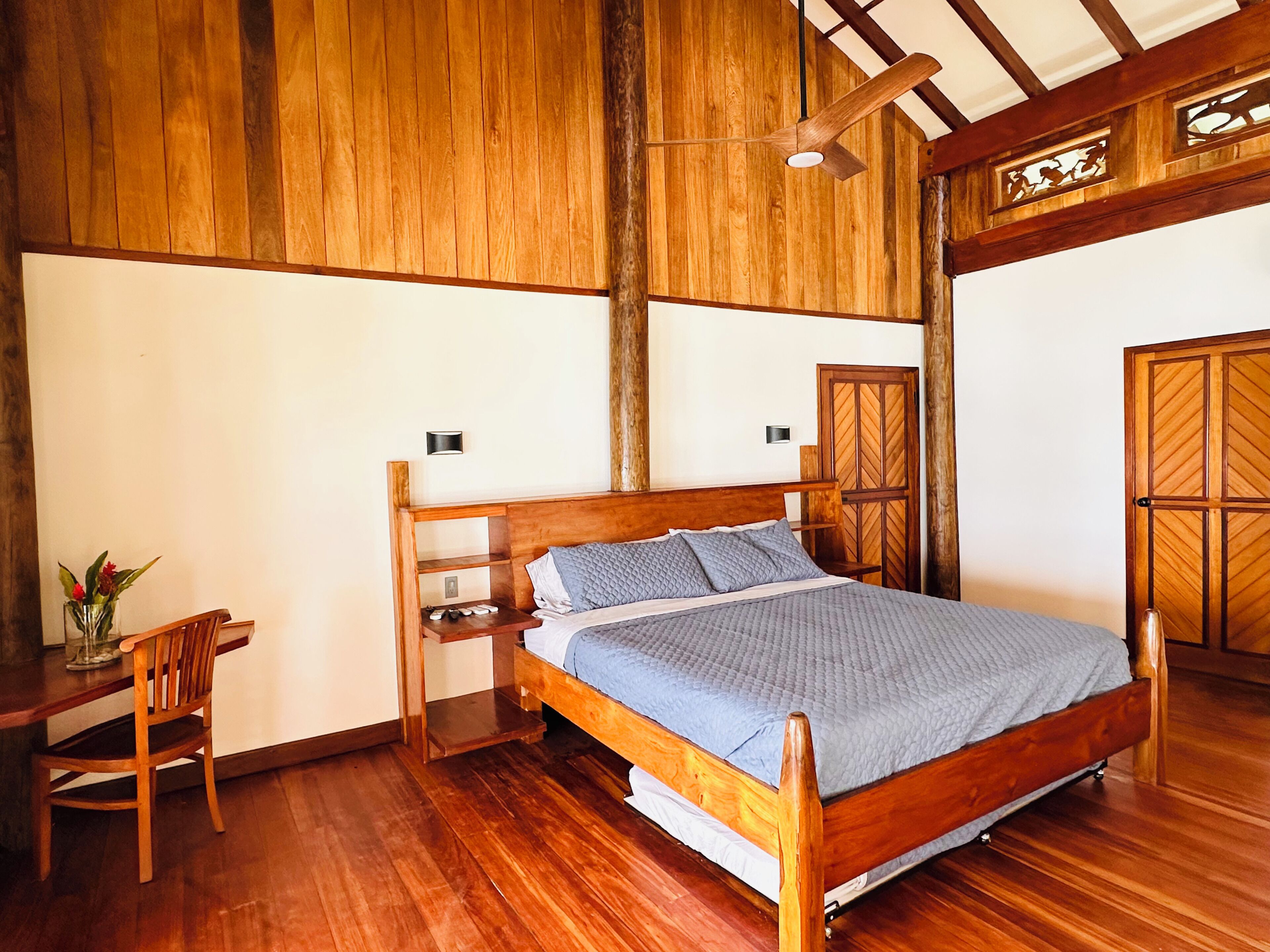 Dormitorio con estructura de madera, cama, mesita de noche, silla y escritorio.