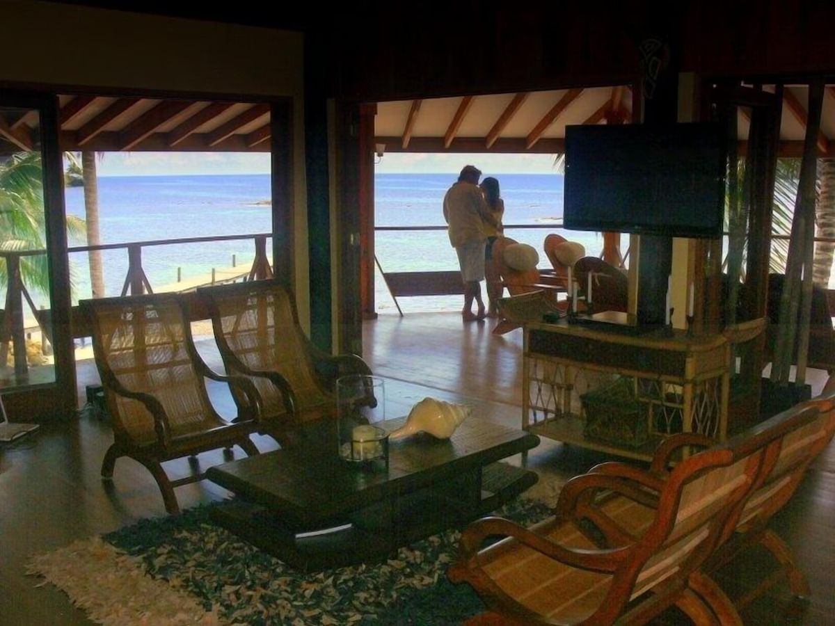 A room with a view of the beach, wooden furniture, a television, and a small table with a candle.