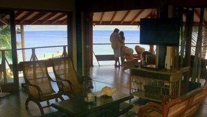 A room with a view of the beach, wooden furniture, a television, and a small table with a candle.