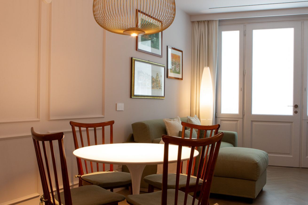 Zona pranzo con tavolo rotondo, quattro sedie, lampadario e divano.