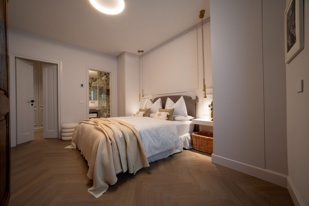 A bedroom with a bed, bedside table, lamp, and a mirror.
