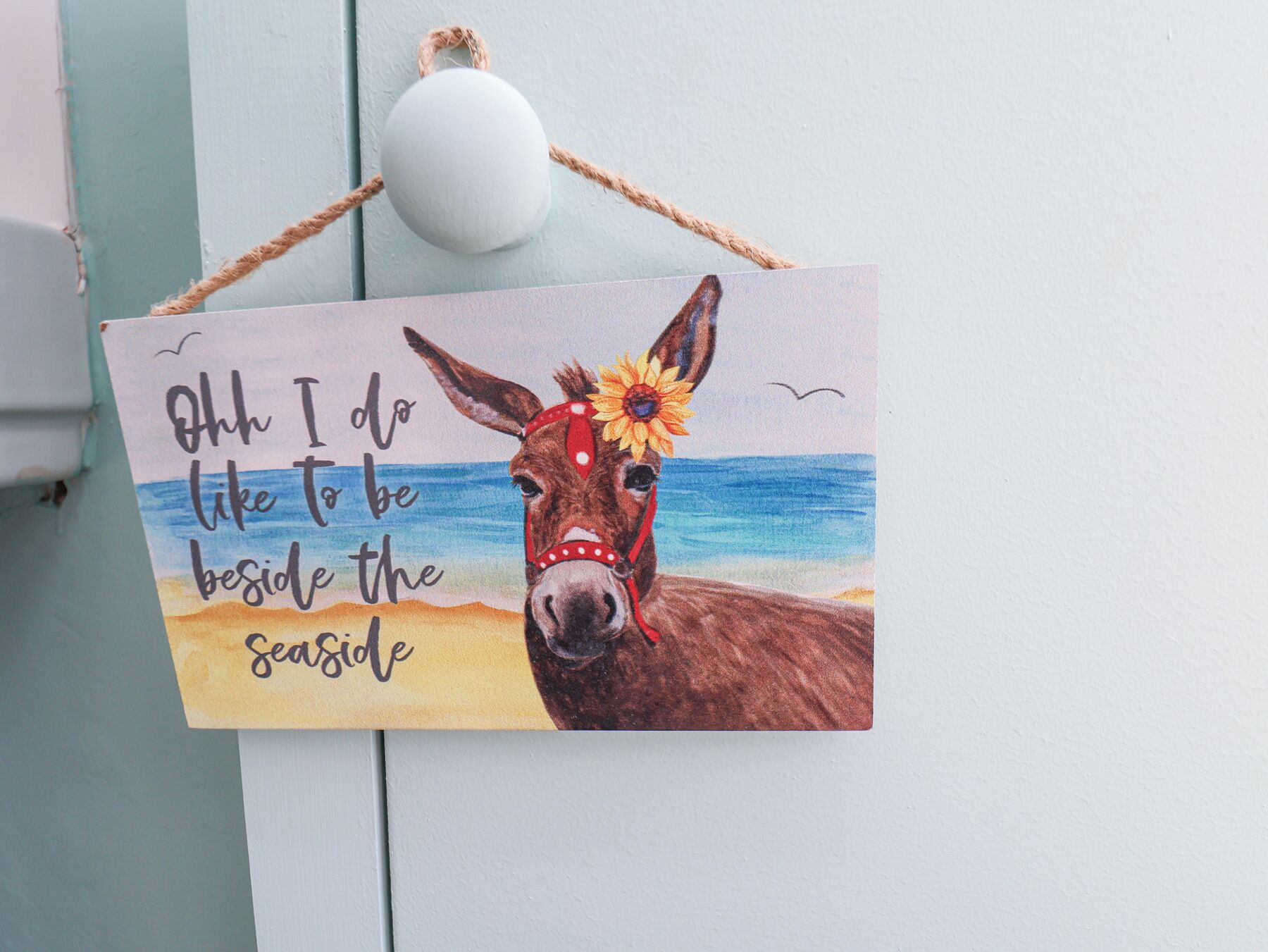 A sign with a horse and a beach scene, featuring the text "Oh I do like to be beside the seaside."
