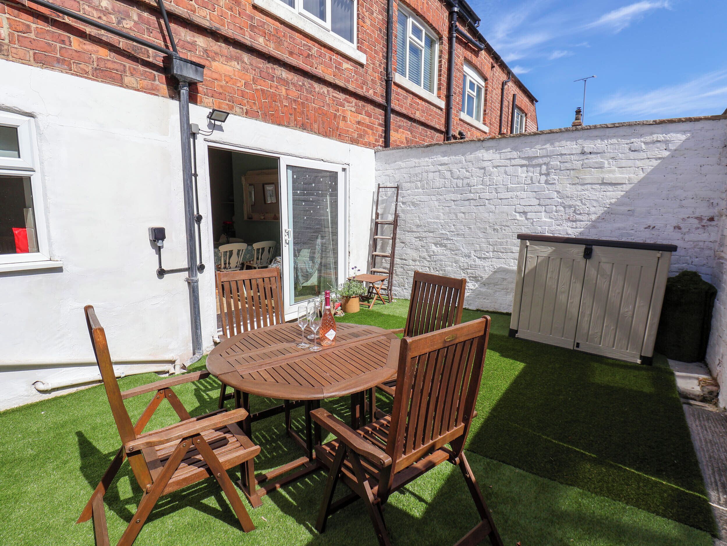 A patio with a round wooden table and chairs, a white door, and a brick wall.