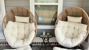 Two wicker chairs with cushions and a small table with drinks on a porch.