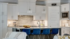A modern kitchen with white cabinets, a central island with bar stools, and a microwave.