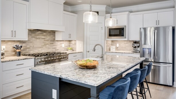 A modern kitchen with white cabinets, a granite island, stainless steel appliances, and pendant lighting.
